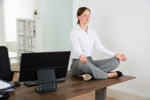 Young Businesswoman Doing Yoga On Wooden Desk In Office